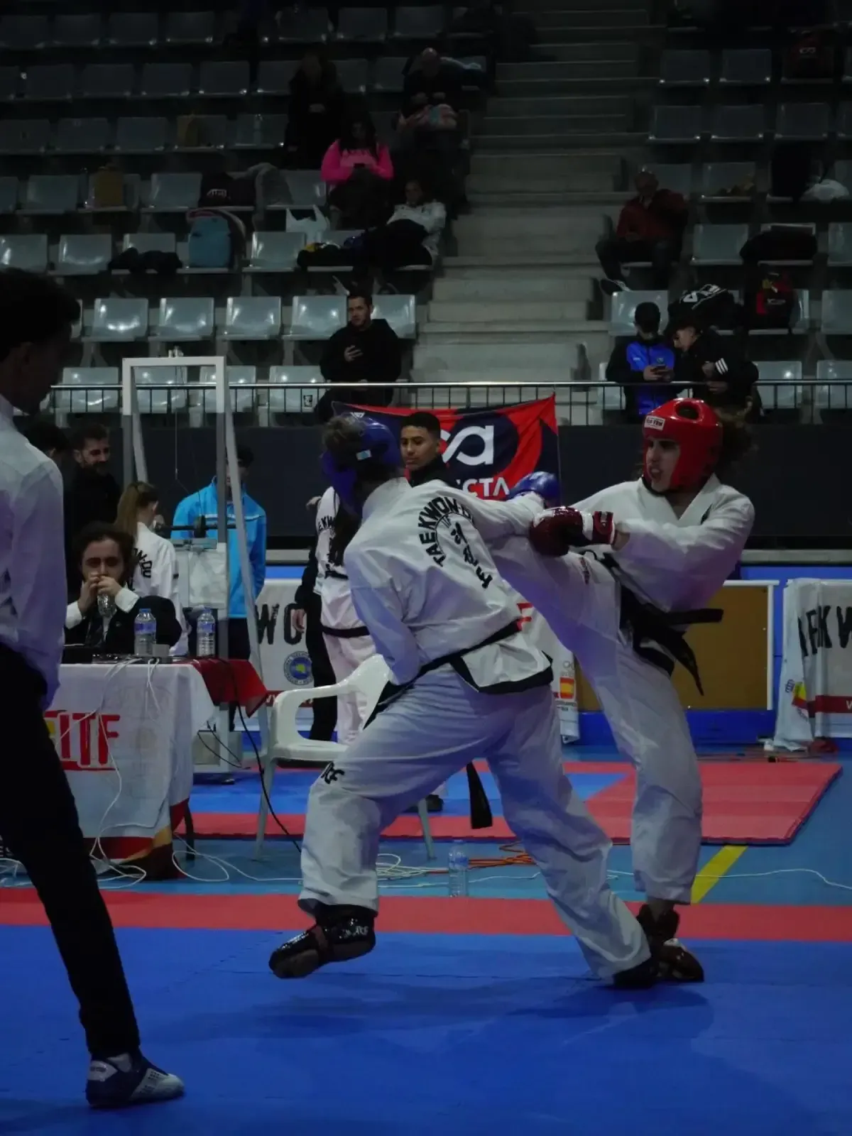 Dos competidores de taekwondo, vestidos con uniformes blancos y equipo de protección, practican sobre una colchoneta azul 