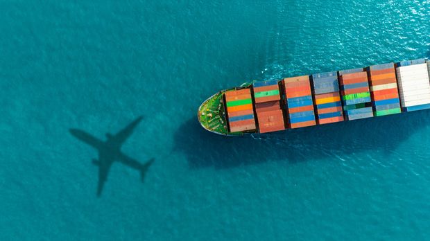 Navire cargo sur une eau turquoise, avec l’ombre d’un avion à proximité