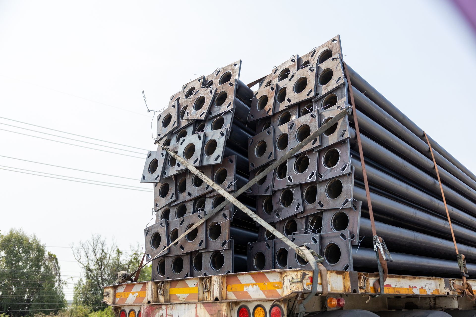 Camion chargé de tubes en acier empilés et de pièces métalliques carrées sur un chantier au bord de la route