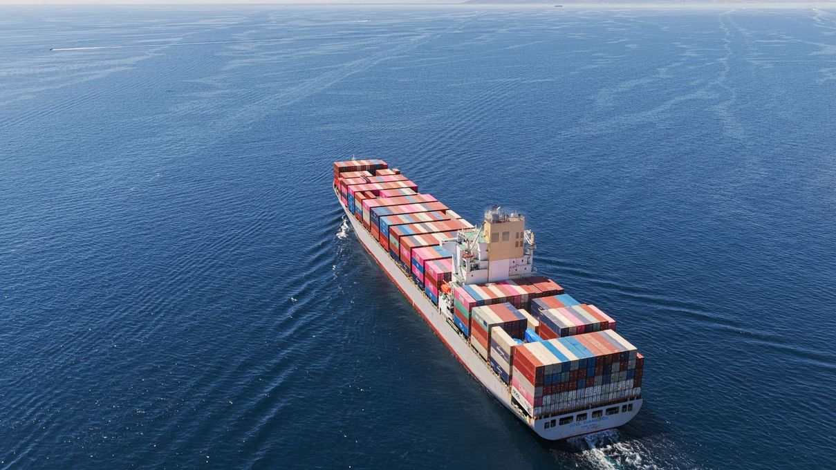 Porte-conteneurs naviguant sur un océan bleu calme, chargé de conteneurs empilés aux couleurs vives