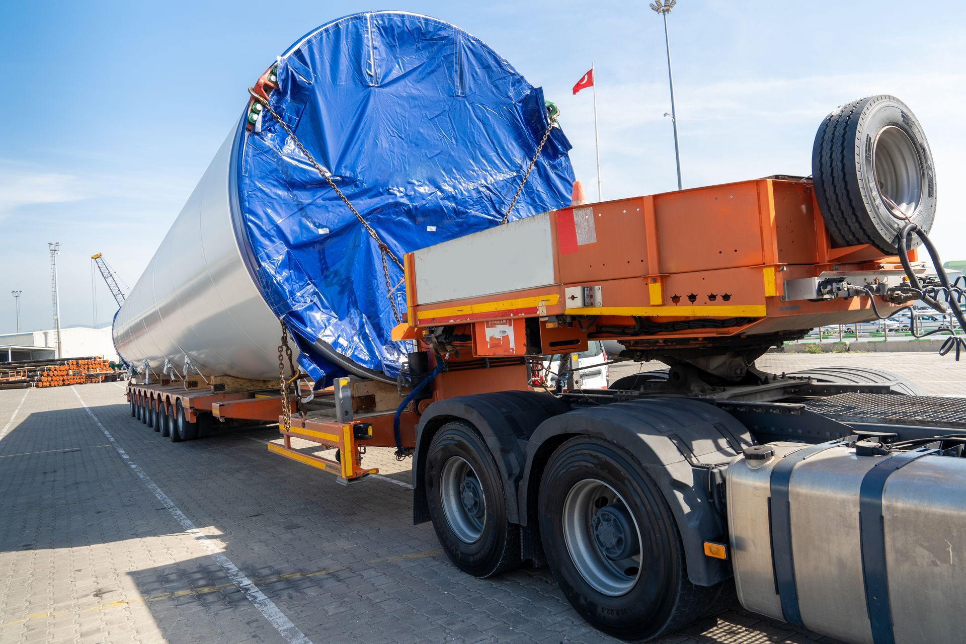 Camion poids lourd transportant une importante cargaison industrielle emballée dans une bâche bleue sur une remorque, au bord d’une route