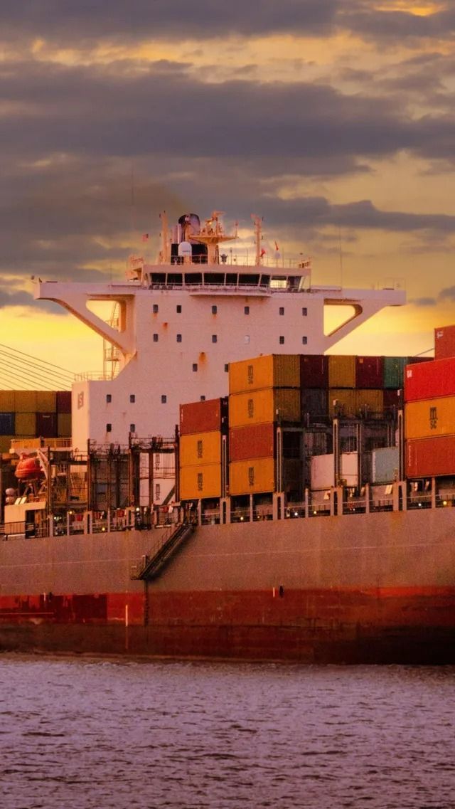 Cargo avec des conteneurs empilés dans un port au coucher du soleil