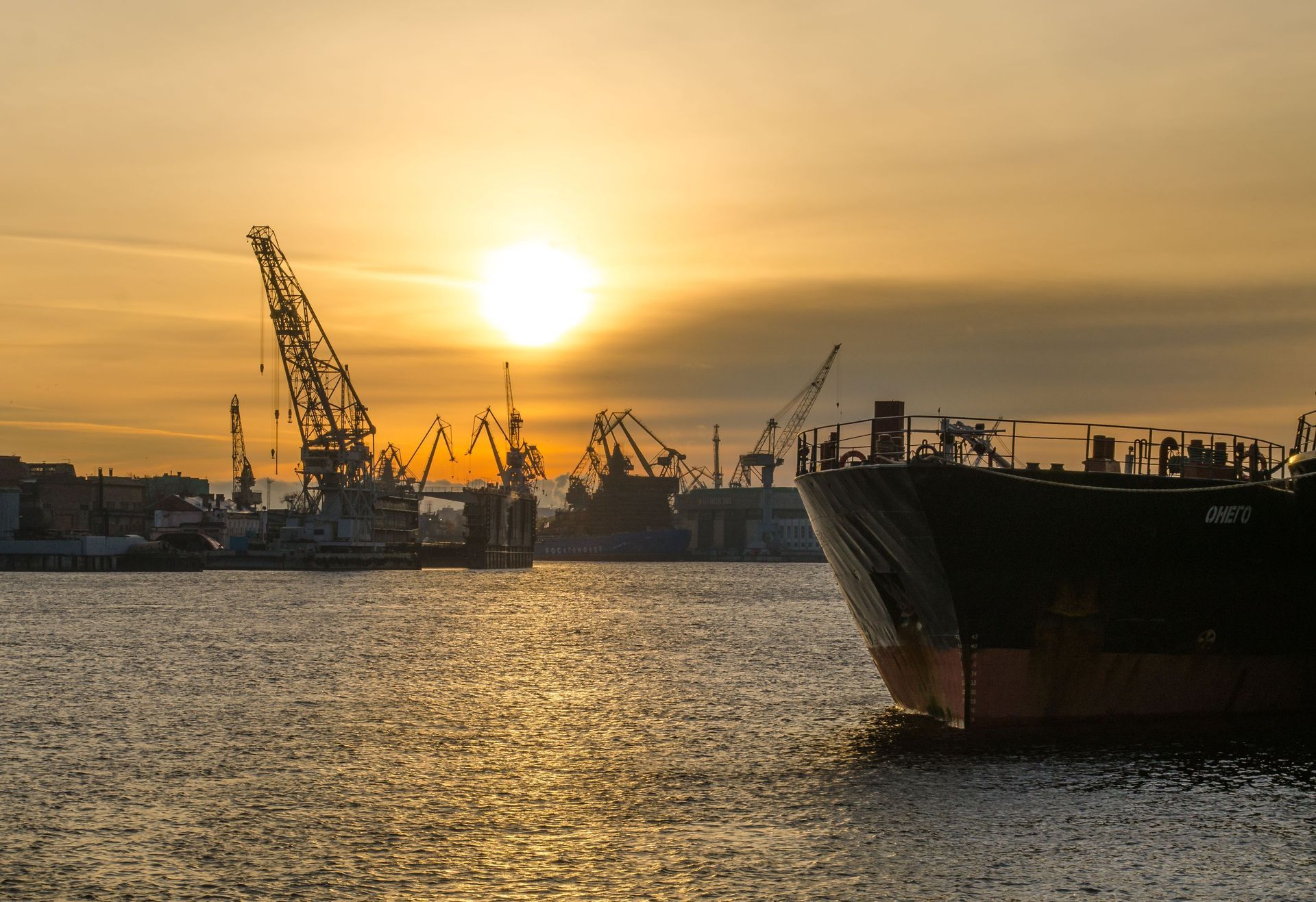 Coucher de soleil sur un port avec des grues, un cargo et des reflets dorés sur l’eau