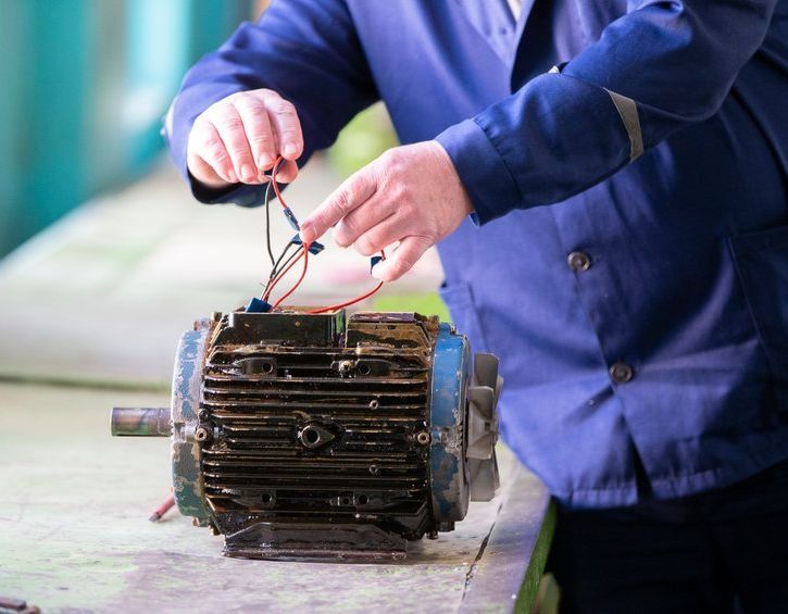 Un hombre con una chaqueta azul está trabajando en un motor eléctrico.