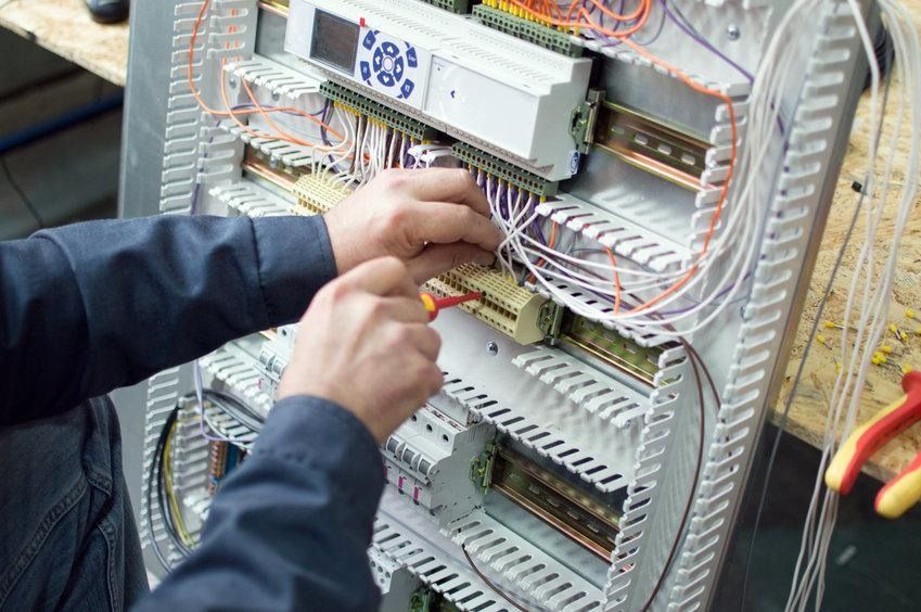 Un hombre está trabajando en un panel eléctrico con un destornillador.