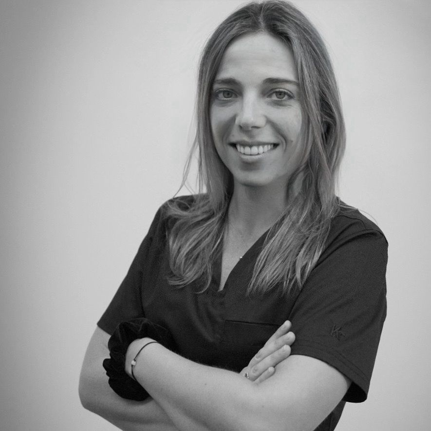 Mujer con los brazos cruzados, sonriente, vestida con un uniforme médico y una goma para el pelo.