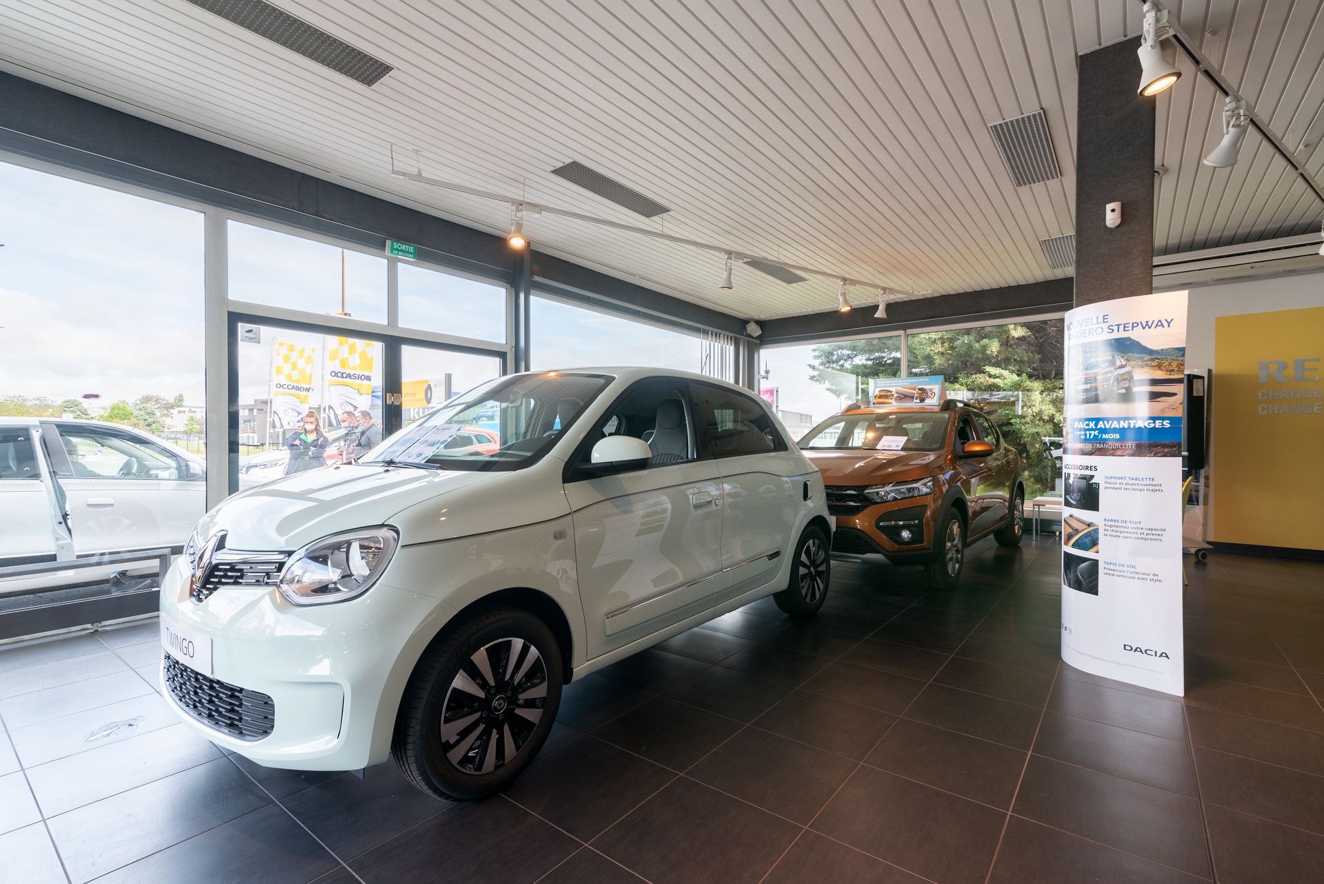 Un SUV blanc dans la salle d'exposition d'un concessionnaire automobile, avec un autre véhicule derrière.