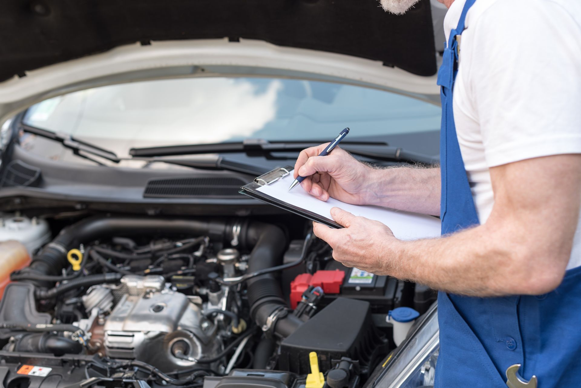 Un mécanicien inspecte le moteur d'une voiture tout en prenant des notes sur un bloc-notes dans un compartiment moteur ouvert.