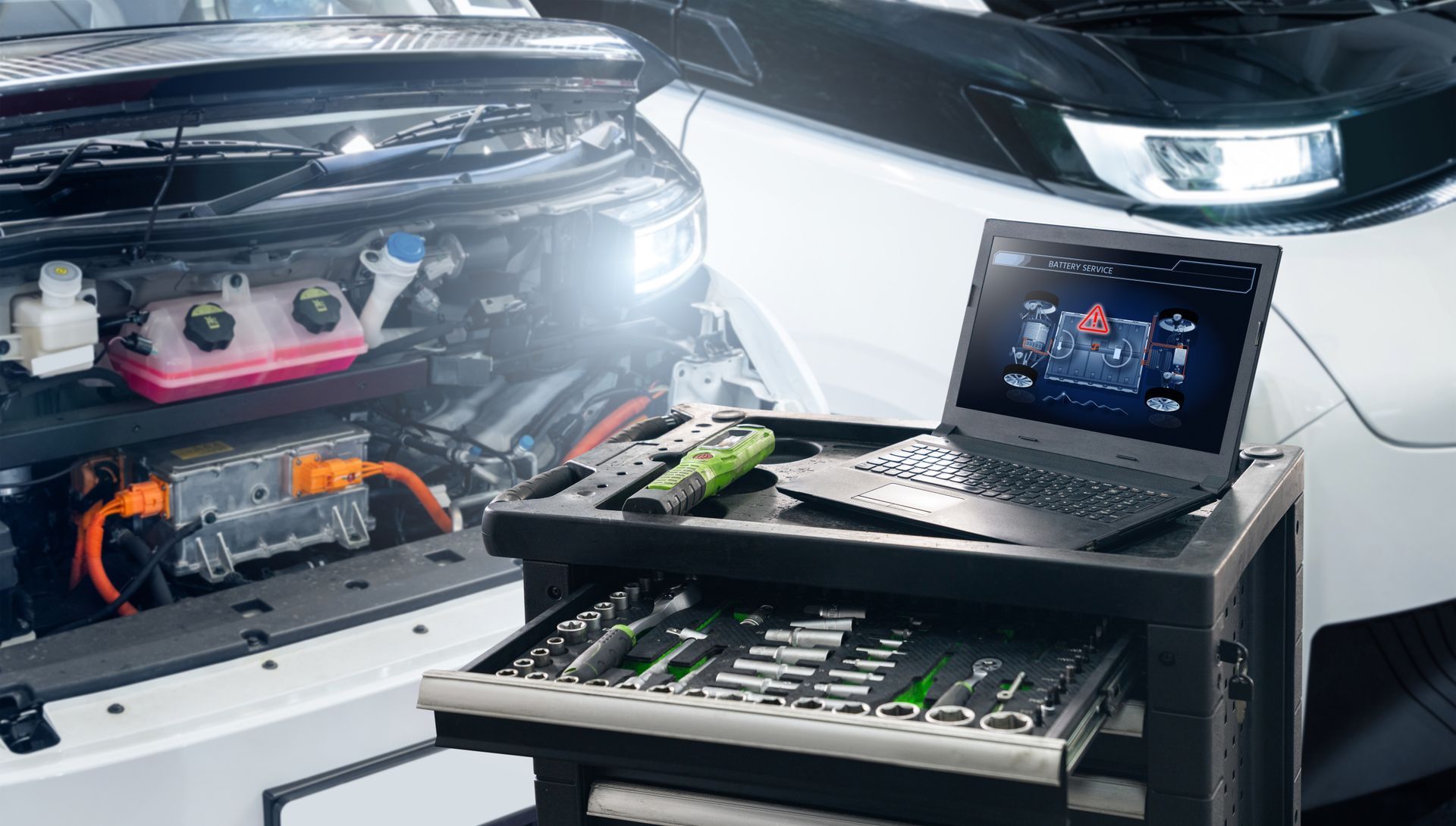 Le compartiment moteur d'une voiture, à côté d'un ordinateur portable et d'un clavier sur un chariot, dans un garage lumineux.