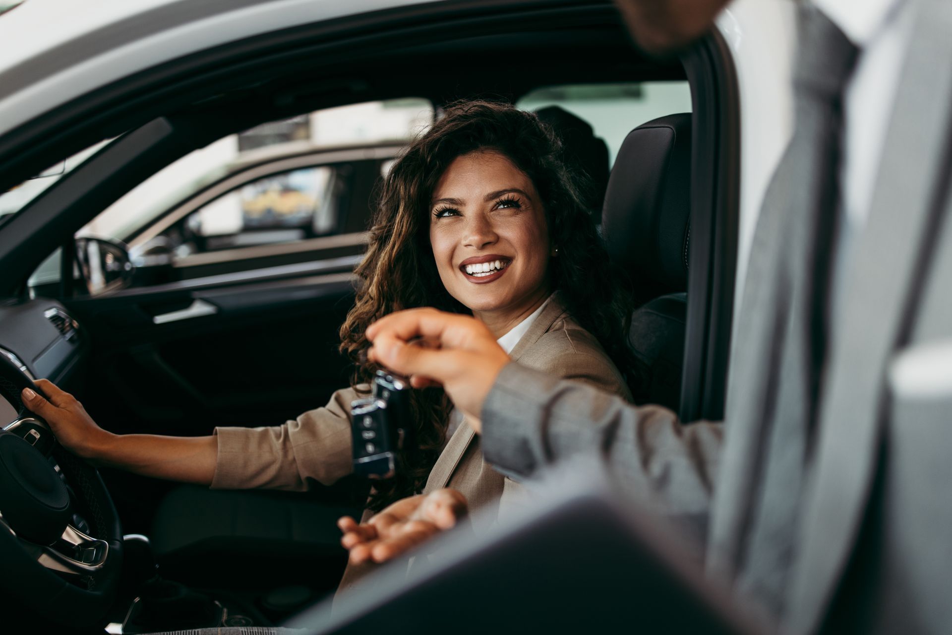 Une femme souriante dans une voiture reçoit les clés d'une personne en costume assise au volant.