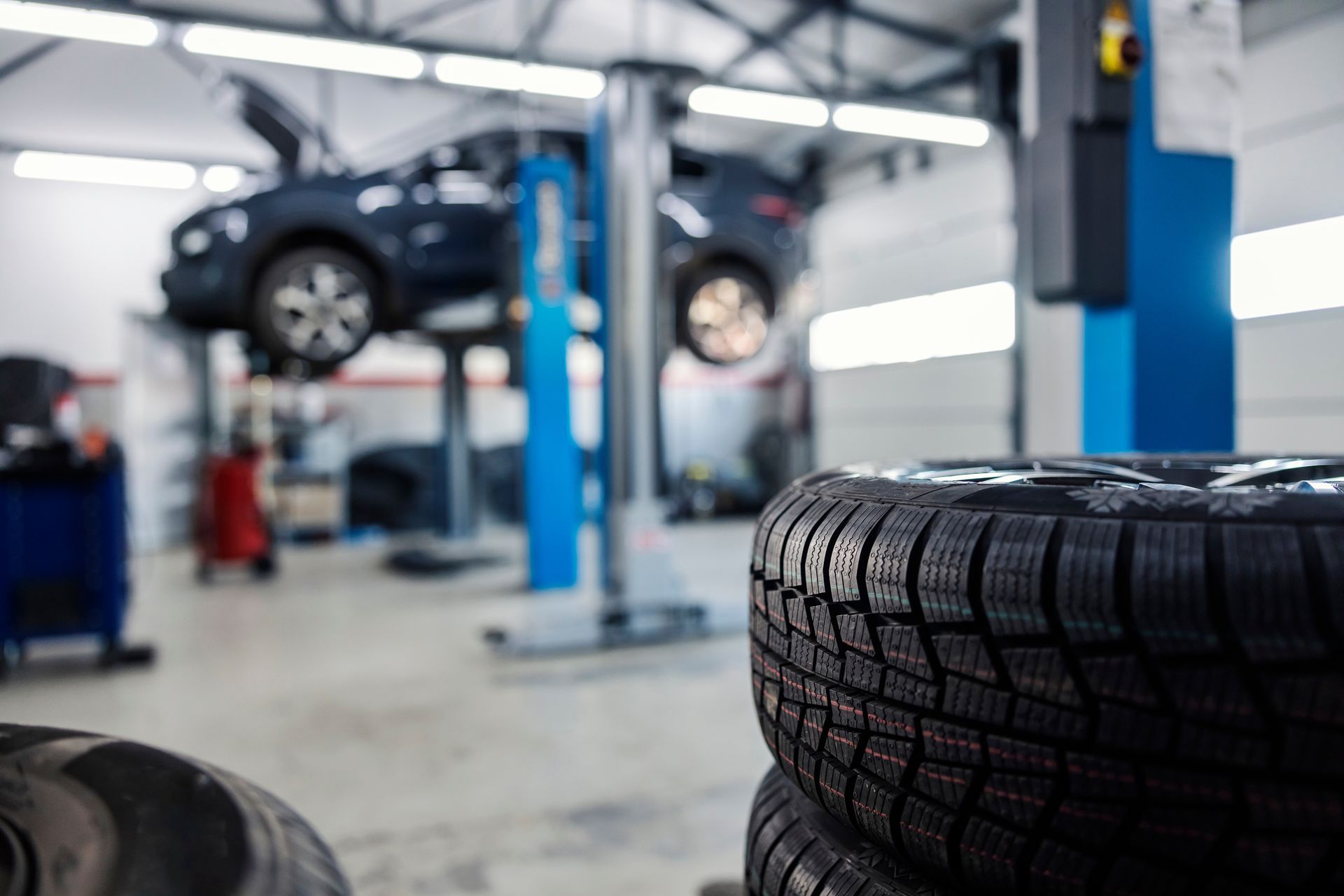 Voiture sur un pont élévateur dans un garage, avec des pneus empilés au premier plan.