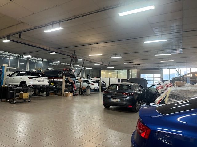 Atelier de réparation automobile avec des voitures sur des ponts élévateurs et des véhicules stationnés dans un atelier lumineux.