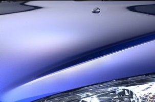 Gros plan sur le capot et le phare d'une voiture bleue avec une petite goutte d'eau dessus.