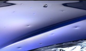Gros plan sur le capot bleu d'une voiture, avec une goutte d'eau et une partie du phare visibles.
