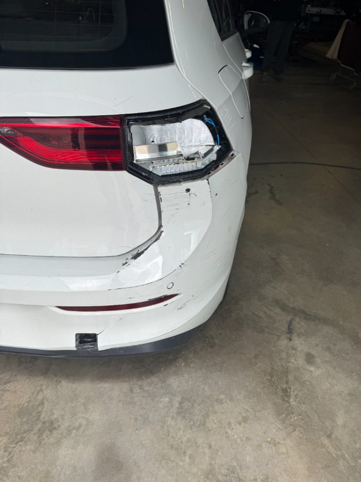 Voiture blanche avec pare-chocs arrière droit et feu arrière endommagés dans un garage.