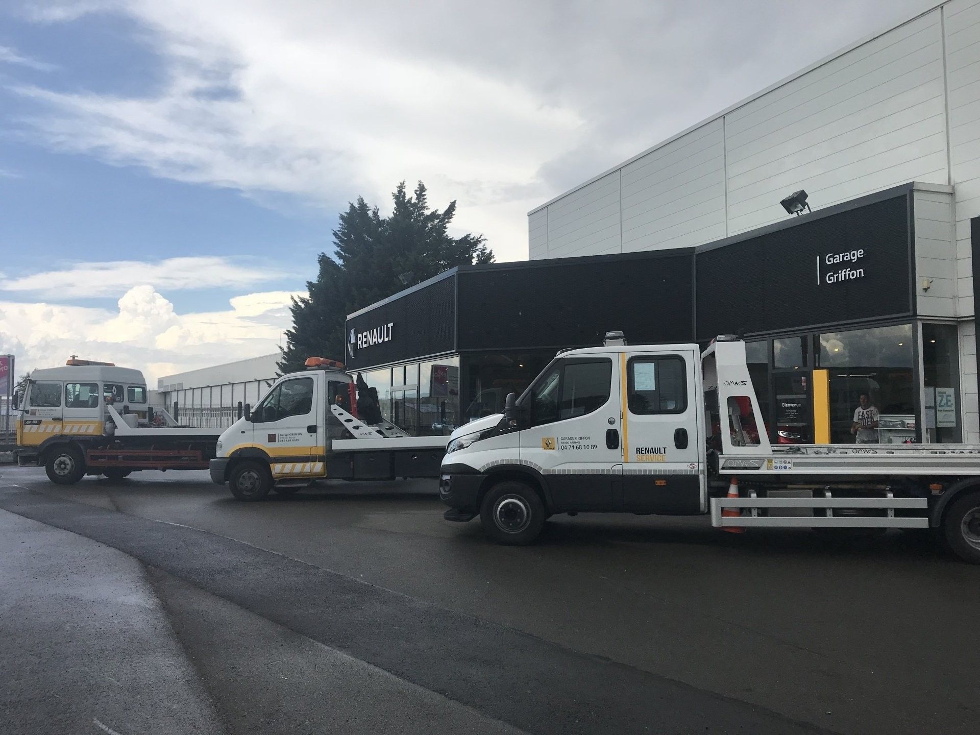 Des camions utilitaires blancs stationnés devant un bâtiment en noir et blanc dans une rue nuageuse.