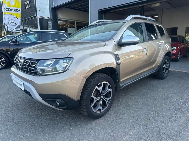 SUV beige stationné devant une concession automobile, vue de trois quarts avant.
