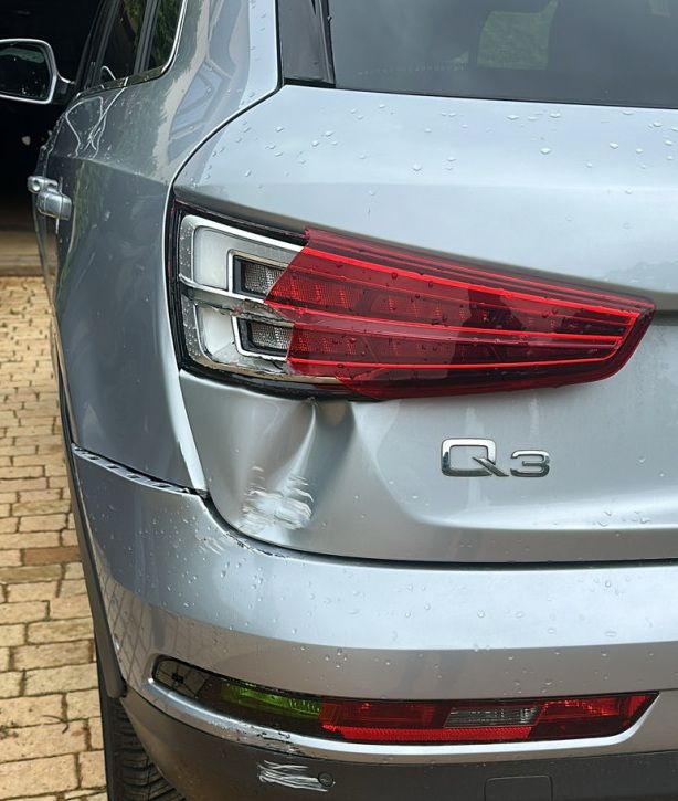 Audi Q3 argentée avec un côté arrière gauche cabossé et un feu arrière endommagé dans une zone de stationnement.