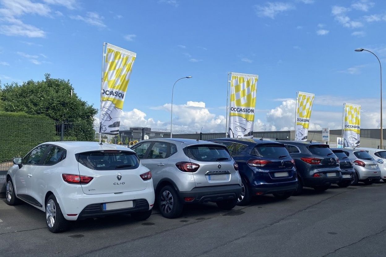Des voitures garées en file indienne le long d'une route, des drapeaux jaunes flottant sous un ciel nuageux.