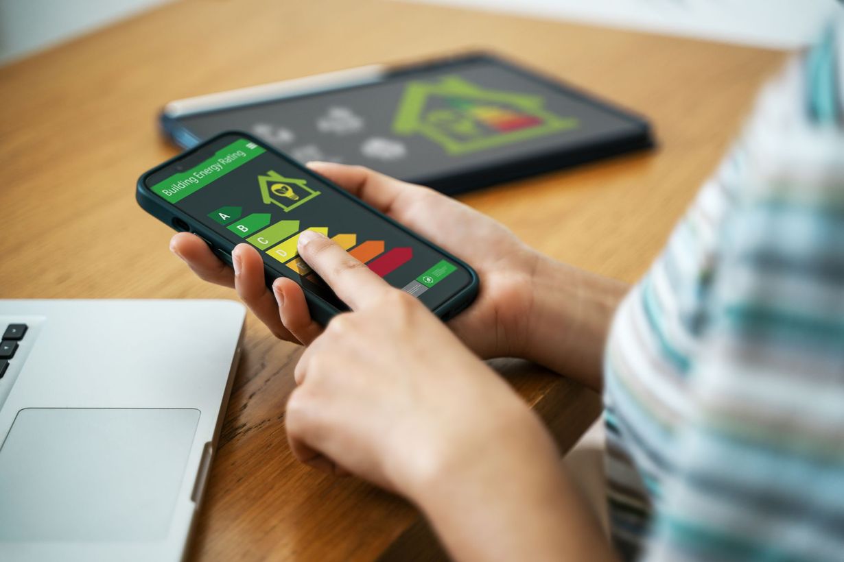 Mains tenant un téléphone avec un écran où sont affichées des étiquettes de classification d'énergie