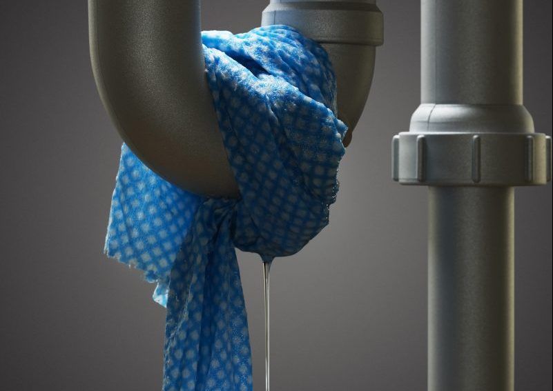 Tissu bleu à motifs noué autour de tuyaux sombres à côté d'un tuyau gris dans un environnement utilitaire