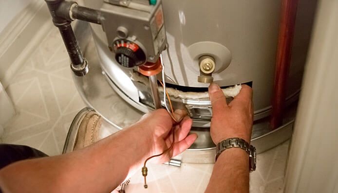 Des mains ajustent le robinet d'un chauffe-eau à l'aide d'outils dans une buanderie.