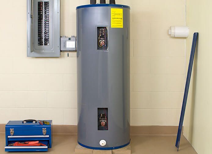 Buanderie avec un grand chauffe-eau à eaux grises, un tableau électrique et des outils adossés à un mur beige.