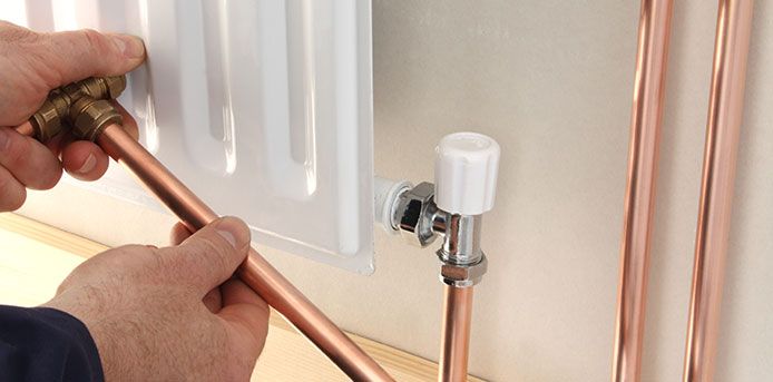 Mains raccordant un tuyau de cuivre à un radiateur blanc à l'aide d'une clé et d'un raccord