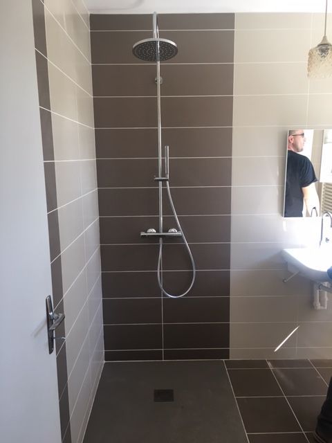 Douche à l'italienne moderne carrelée avec pommeau de douche fixe et douchette, lavabo blanc et miroir sur la droite