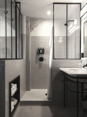 Douche moderne avec paroi de verre à cadre noir, carrelage blanc et lavabo sur la droite