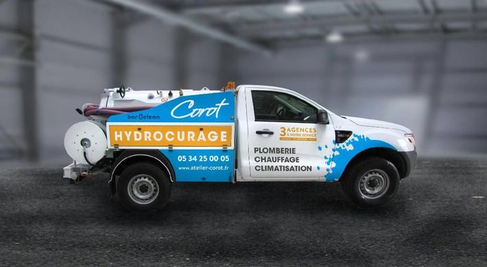Camion de course bleu et blanc avec des autocollants de sponsors sur un sol sombre, sur fond gris flou.