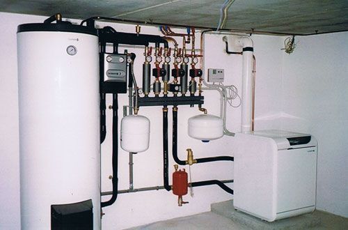 Local technique au sous-sol avec chauffe-eau, chaudière, tuyauterie, vannes et équipements utilitaires