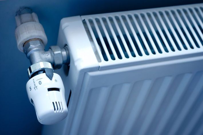 Gros plan sur un robinet thermostatique de radiateur blanc dans une pièce aux tons bleutés