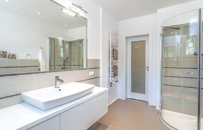 Salle de bains moderne et lumineuse avec meuble-lavabo blanc, grand miroir, douche en verre et carrelage beige au sol