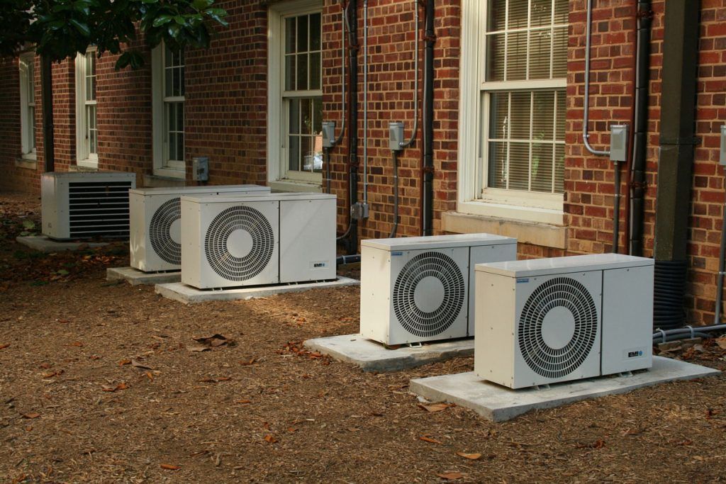 Trois unités de climatisation extérieures à côté d'un bâtiment en briques avec des fenêtres.
