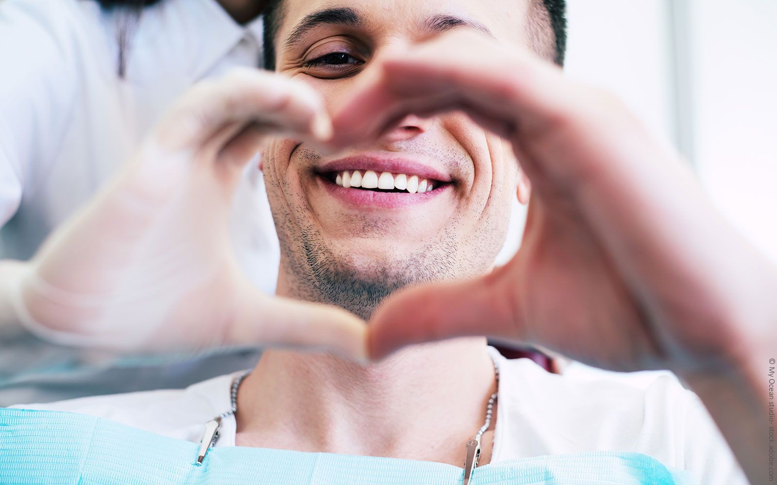 Ein Mann formt mit seinen Händen ein Herz, während er auf einem Zahnarztstuhl sitzt.