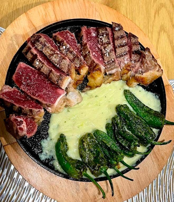 Un plato de filete y pimientos verdes sobre una mesa de madera.