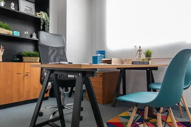 Una habitación con un escritorio, sillas y una estantería.