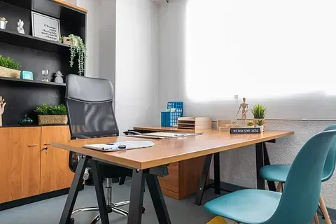 Una oficina en casa con un escritorio, sillas, estantes y una ventana.