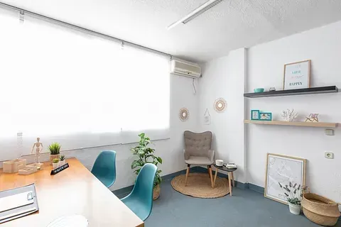 Una habitación con un escritorio, sillas, estantes y una ventana.