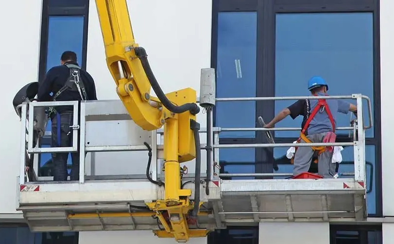 Deux laveurs de vitres sur une nacelle blanche nettoient de grandes fenêtres sur un bâtiment blanc.