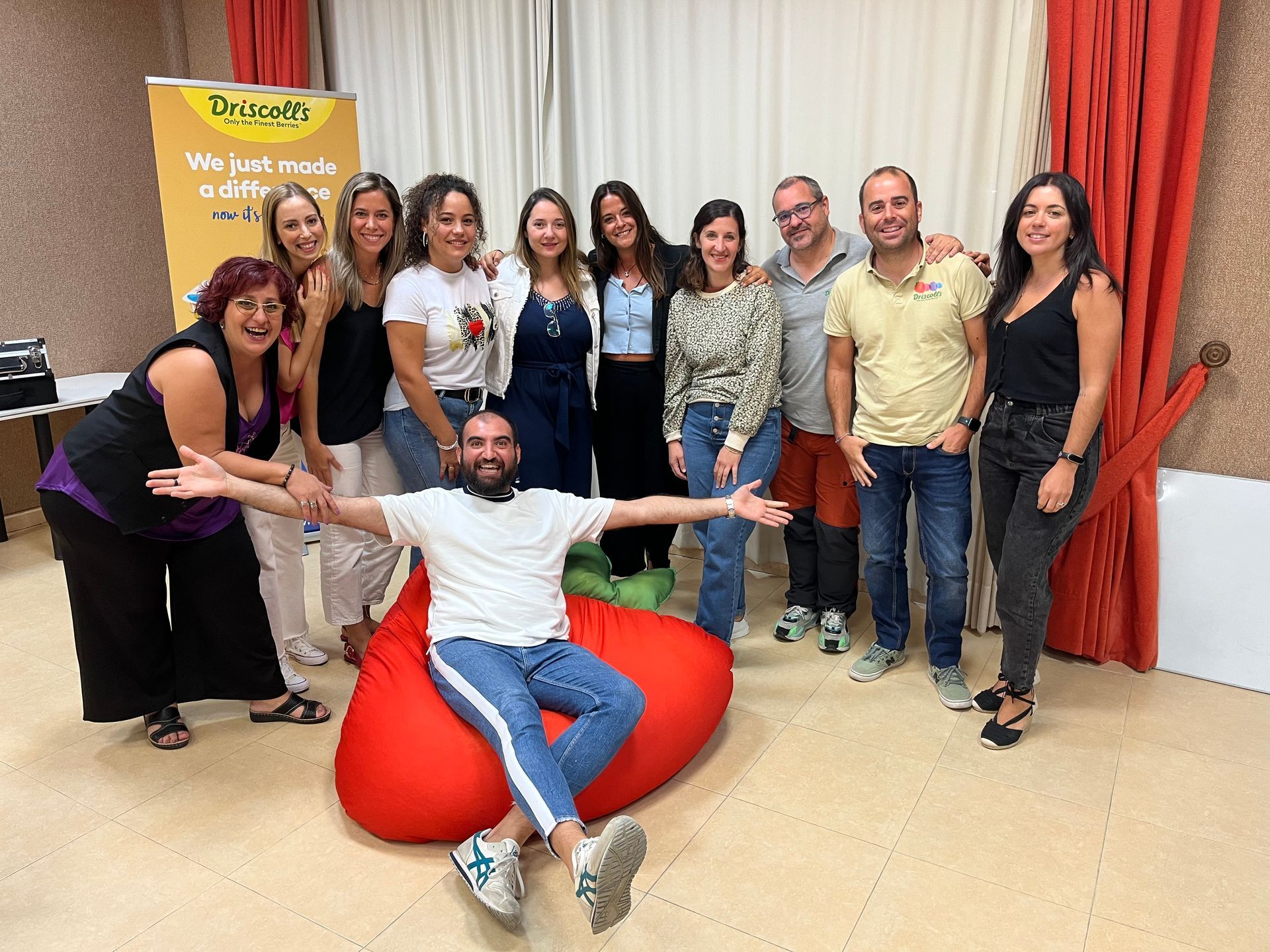 Un grupo de personas posa para una fotografía en una habitación con un hombre sentado en un sillón puf.