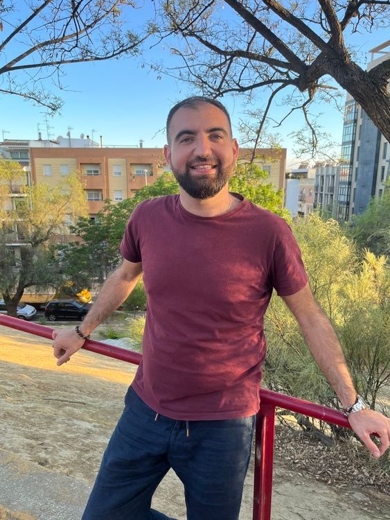 Un hombre con barba está de pie junto a una barandilla en un parque.