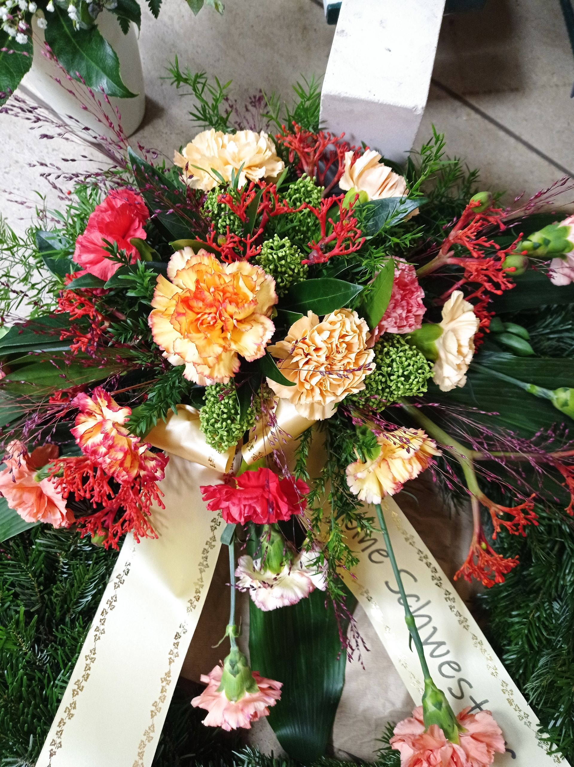 Kranz aus orangefarbenen, rosa und roten Nelken mit einer Schleife.