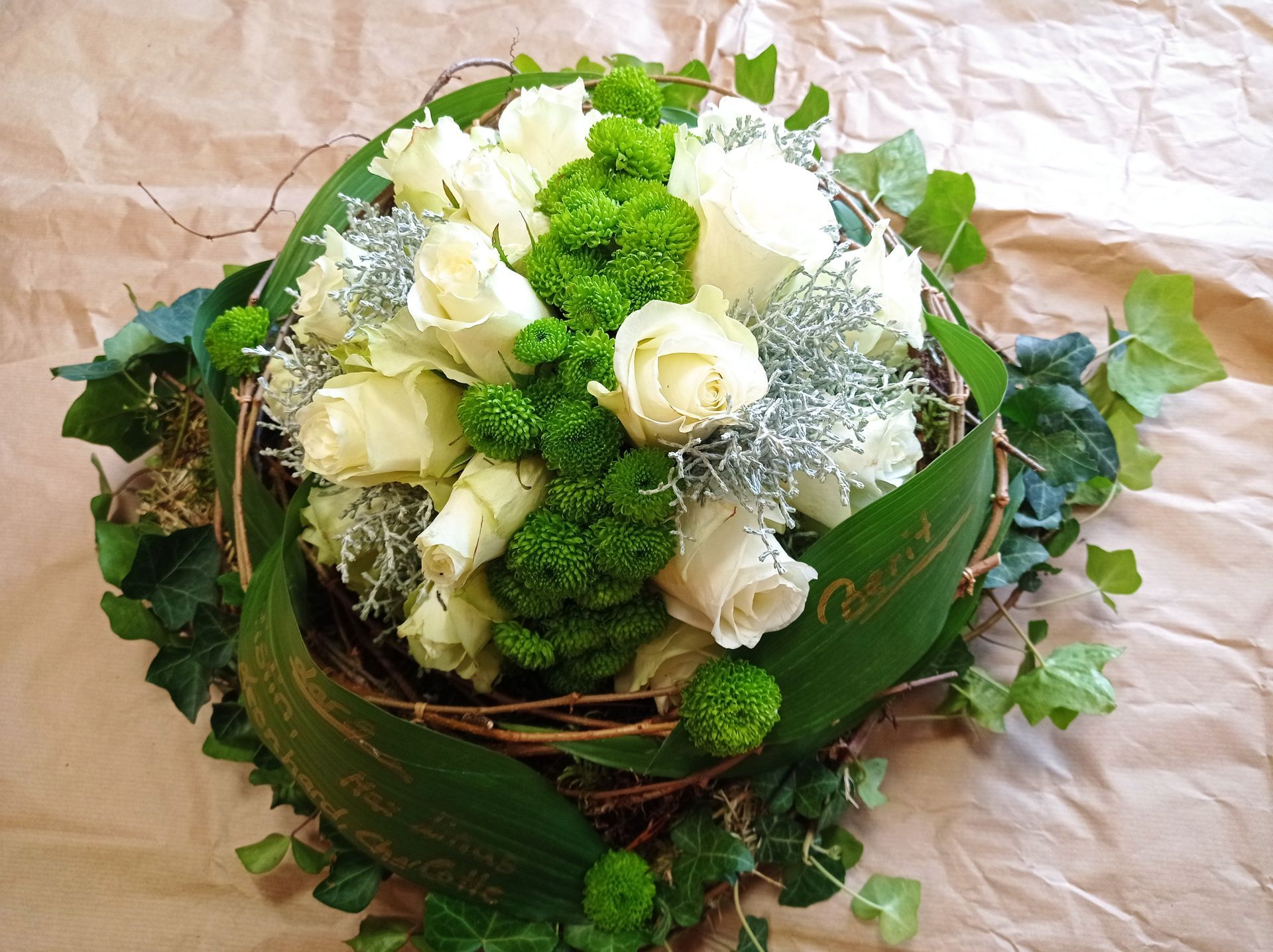 Weiße Rosen, grüne Chrysanthemen und Blätter in einem geflochtenen Nest auf braunem Papier.
