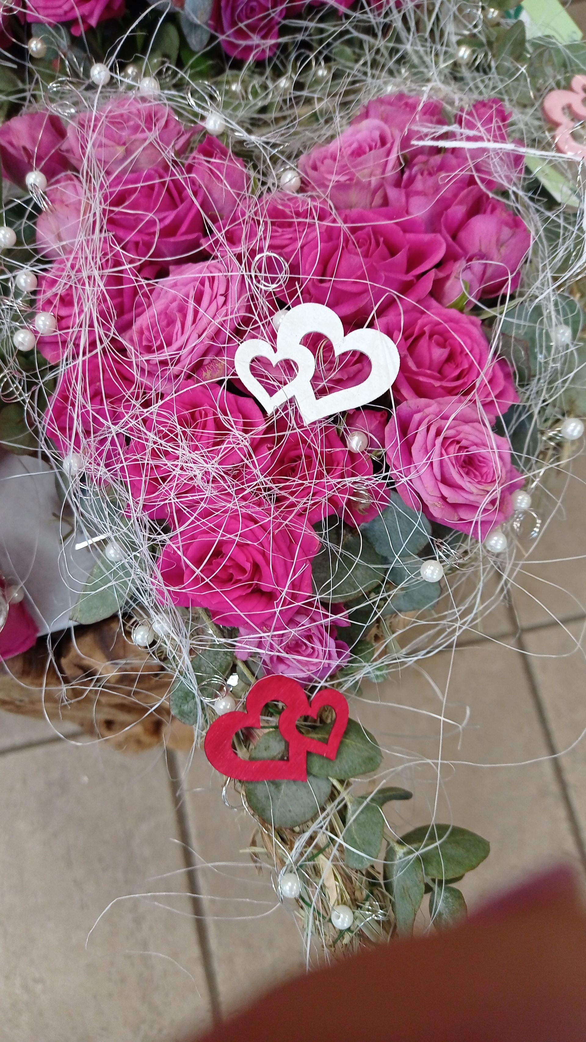 Herzförmiger Strauß aus rosa Rosen, verziert mit Silberdraht und weißen und roten Herzornamenten.