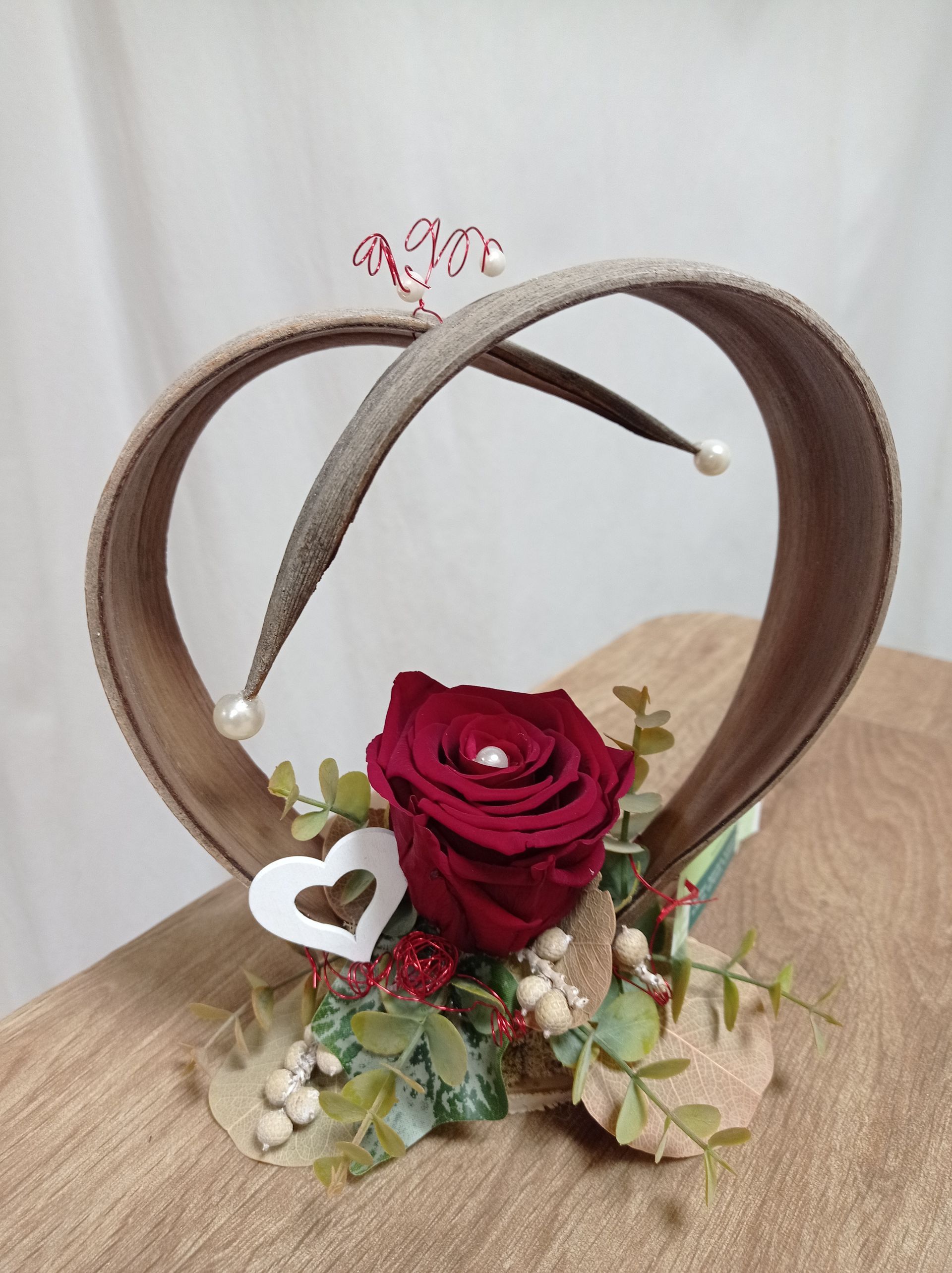 Tafelaufsatz aus roten Rosen mit braunem Herzrahmen, weißem Herz und dekorativem Blattwerk.