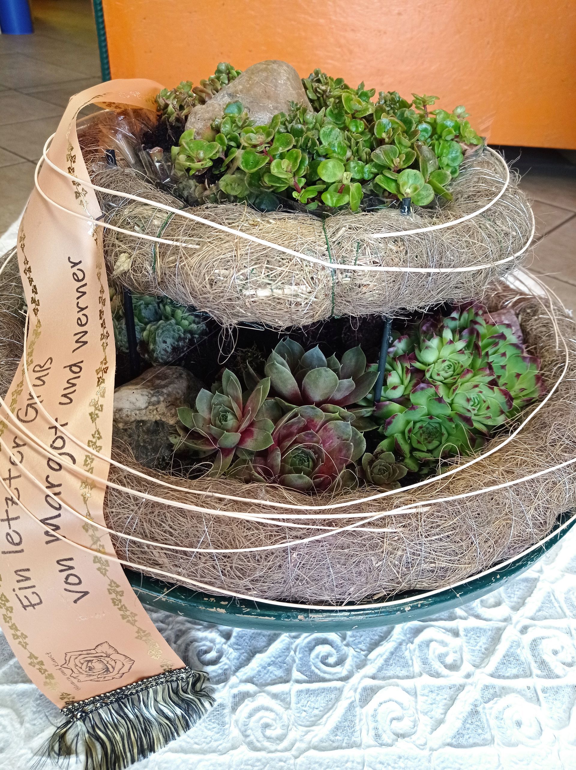 Tiered succulent arrangement with sand, rocks, and a banner that says