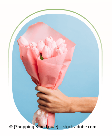 Eine Hand hält einen Strauß rosa Tulpen, die in rosa Papier gewickelt sind, vor blauem Hintergrund.