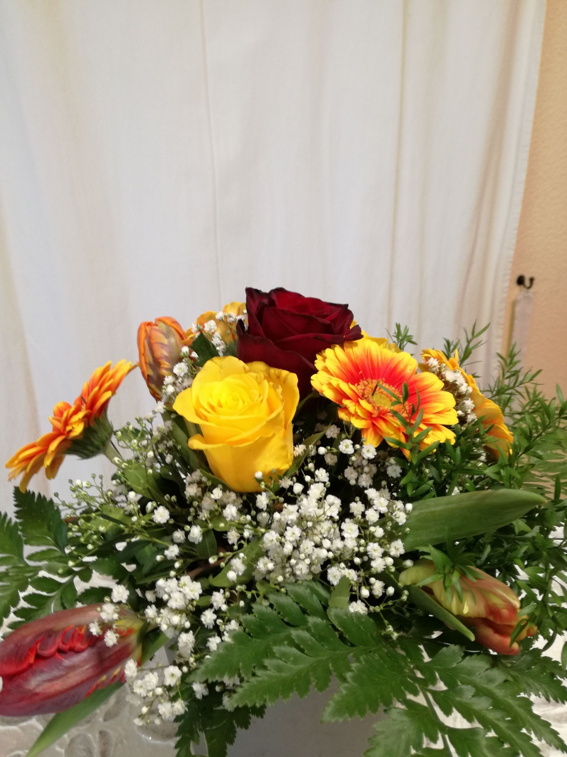 Ein farbenfrohes Blumenarrangement mit einer roten Rose und Tulpen, einer gelben Rose und orangefarbenen Gänseblümchen vor weißem Hintergrund.